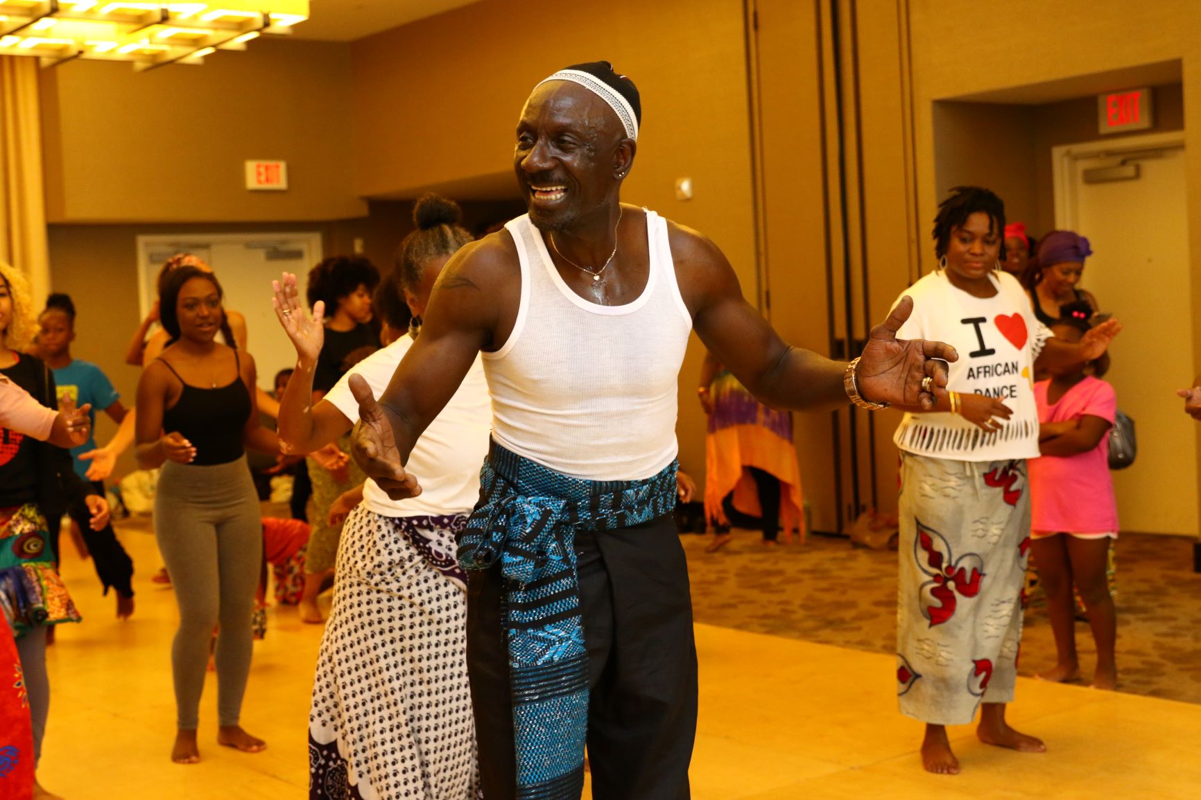 Man in white shirt and blue print pants teaching African dance class